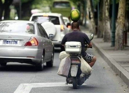 把西瓜顶在头上骑摩托的男子